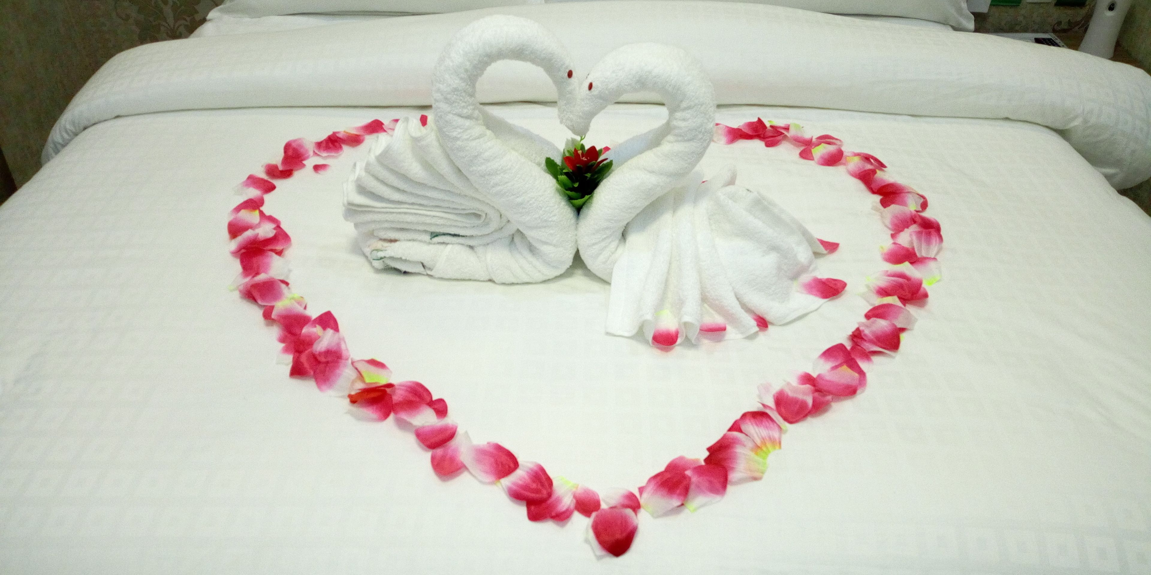 A bed with a heart-shaped arrangement of towels and rose petals.