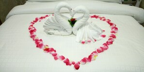 A bed with a heart-shaped arrangement of towels and rose petals.