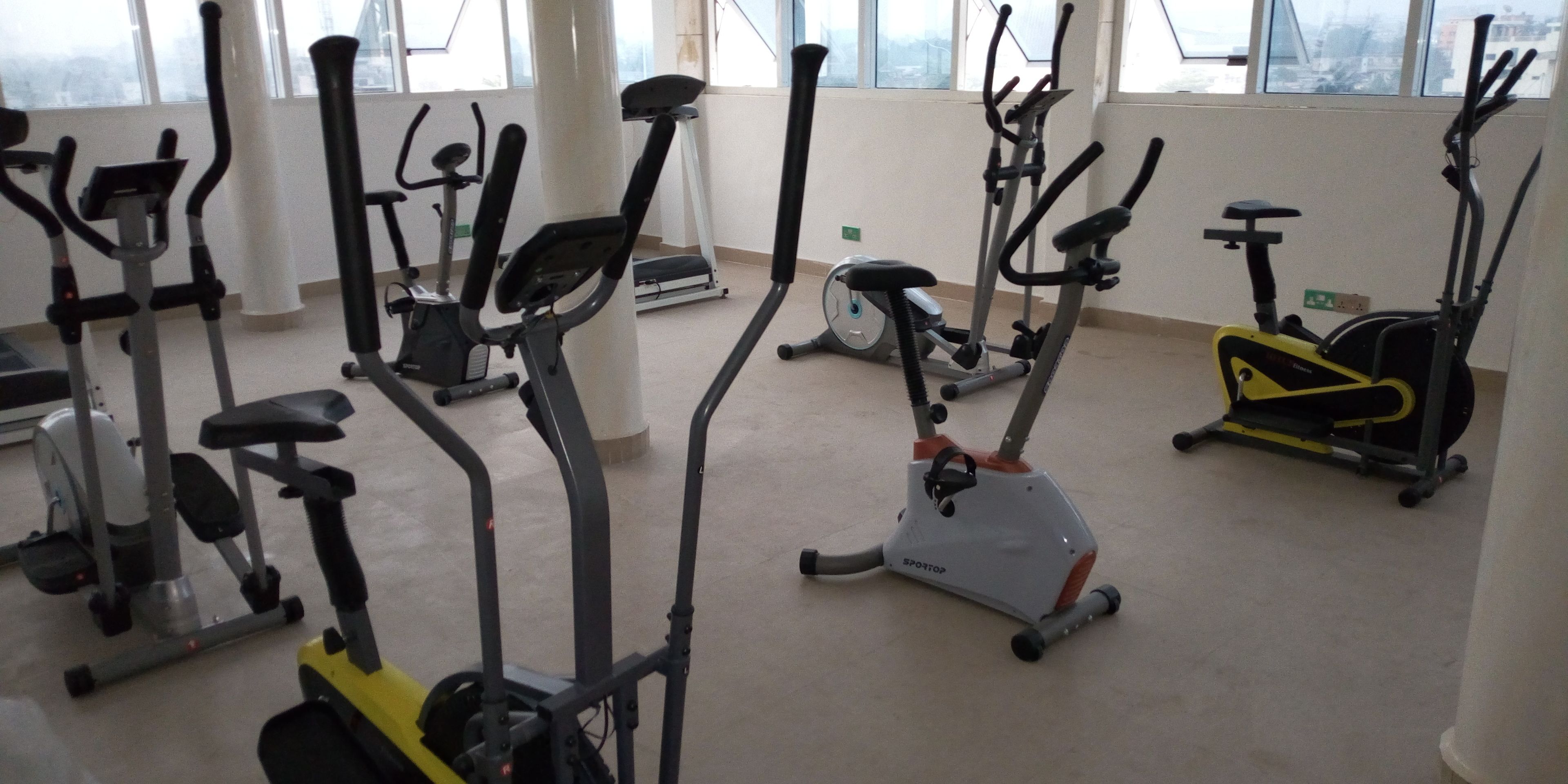 A gym with various stationary bikes and treadmills, large windows, and a high ceiling.