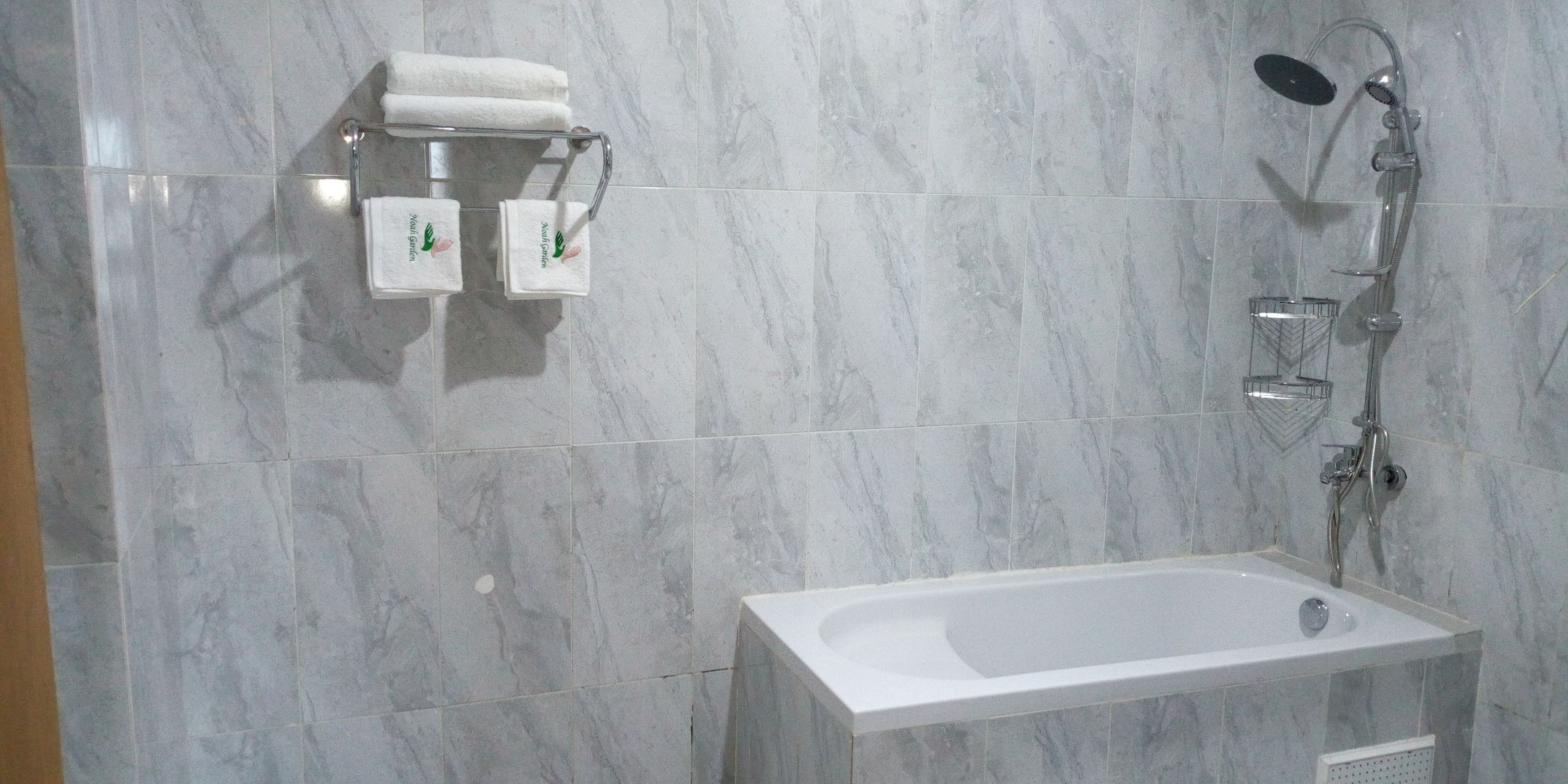 A bathroom with a marble floor, a white bathtub, and a shower with a handheld showerhead.