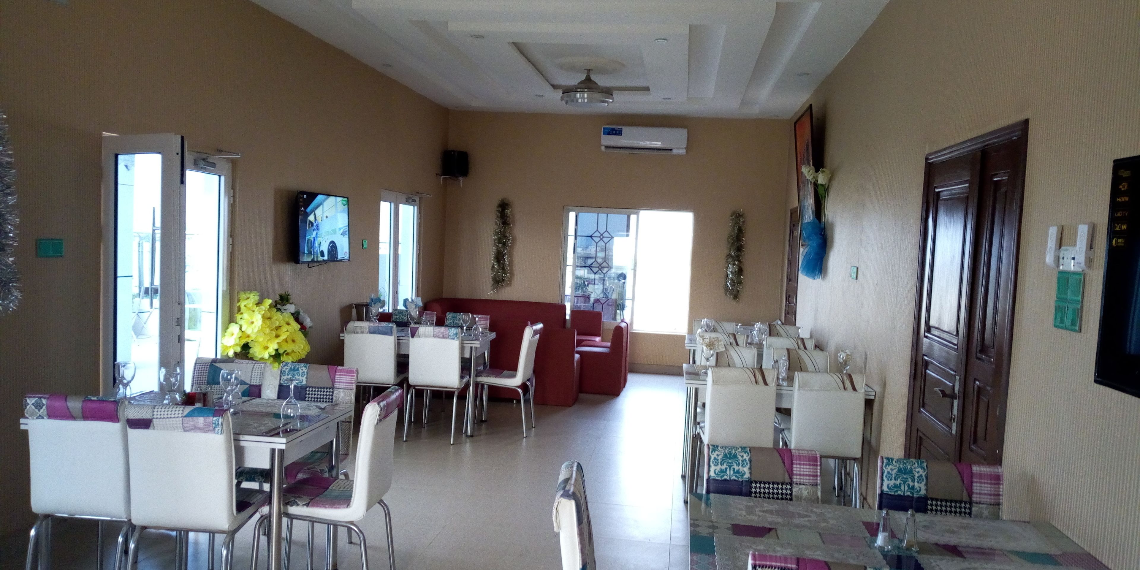 A dining area with multiple tables and chairs, a television mounted on the wall, and a ceiling fan.