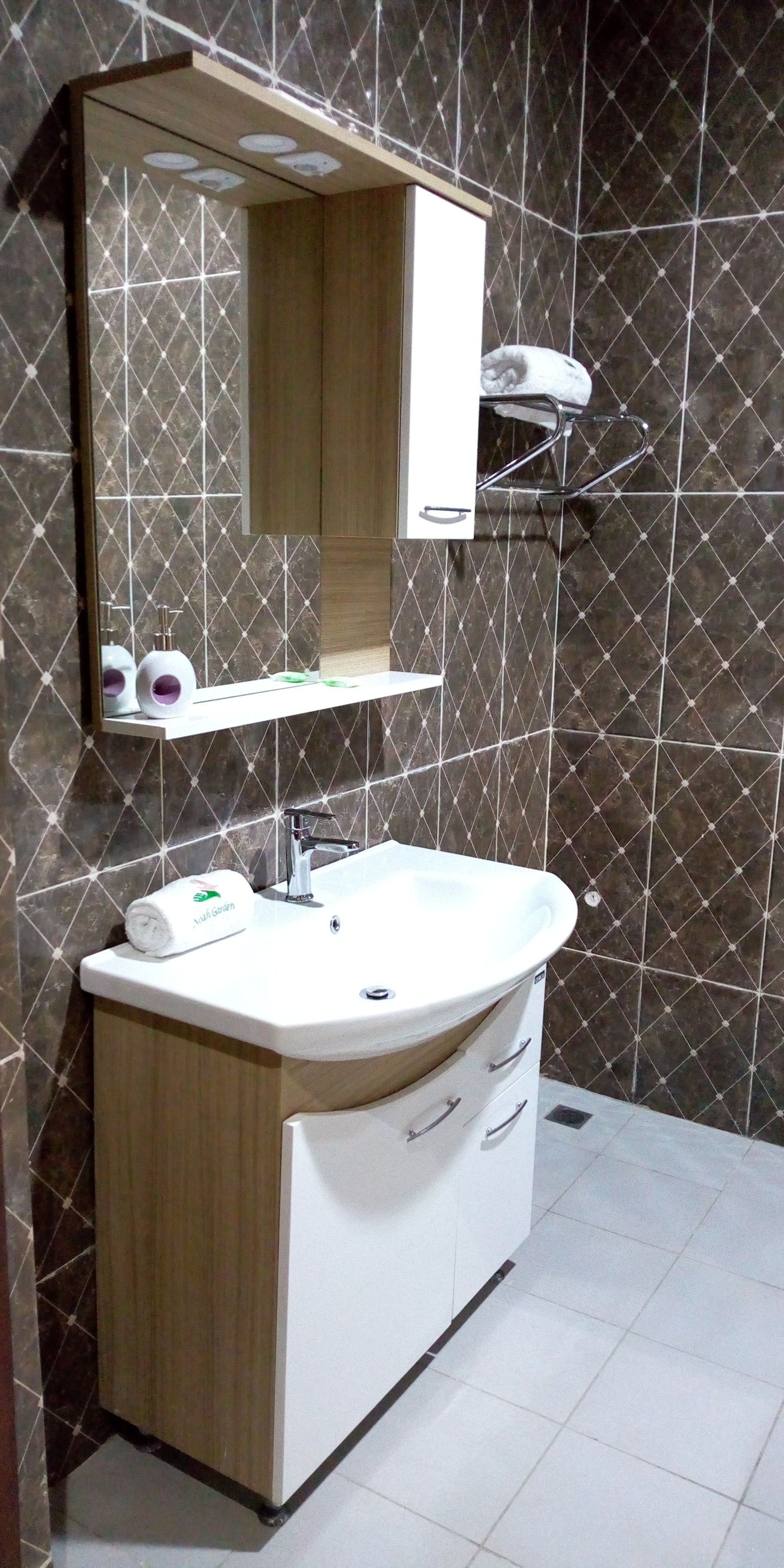 Un baño con un lavamanos blanco, un espejo encima y una toalla colgada en un perchero.