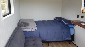 Una habitación pequeña con cama, un banco, una ventana y una mesita de noche con lámpara.