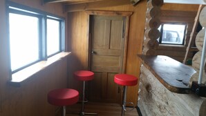 Un interior de madera con una puerta, dos taburetes rojos y una ventana.