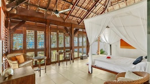 A room with a bed, a chair, a table, and a window with a view of the beach.