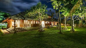 A traditional-style building with a thatched roof, surrounded by a well-maintained lawn and several trees. - House of Palms (Teouma)
