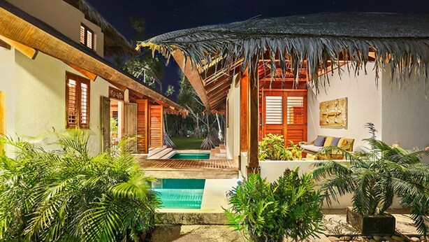 A tropical resort with a pool, thatched-roof structures, and lush greenery.