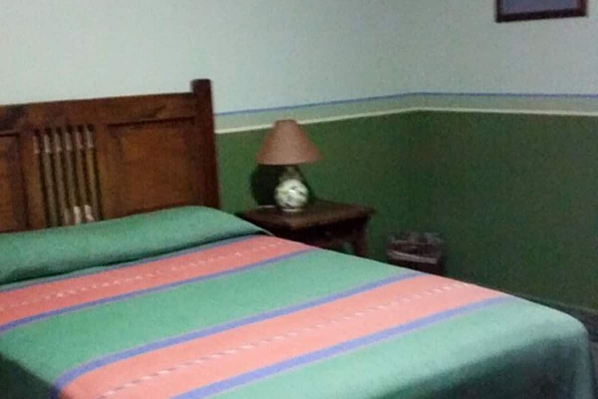 Una habitación con una cama, una mesita de noche, una lámpara y un cuadro en la pared.