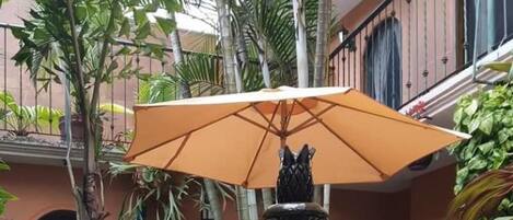 Un patio con una fuente central, rodeado de abundante vegetación y sillas blancas.