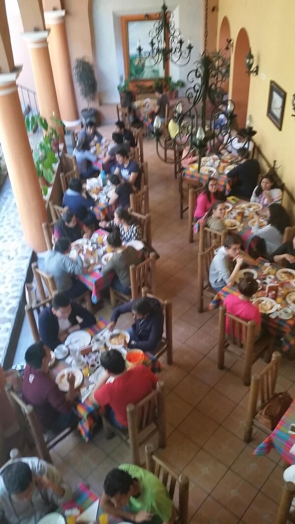 A dining area with multiple tables and chairs, people seated and eating.