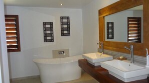 A modern bathroom with a freestanding bathtub, two sinks, and a large mirror.