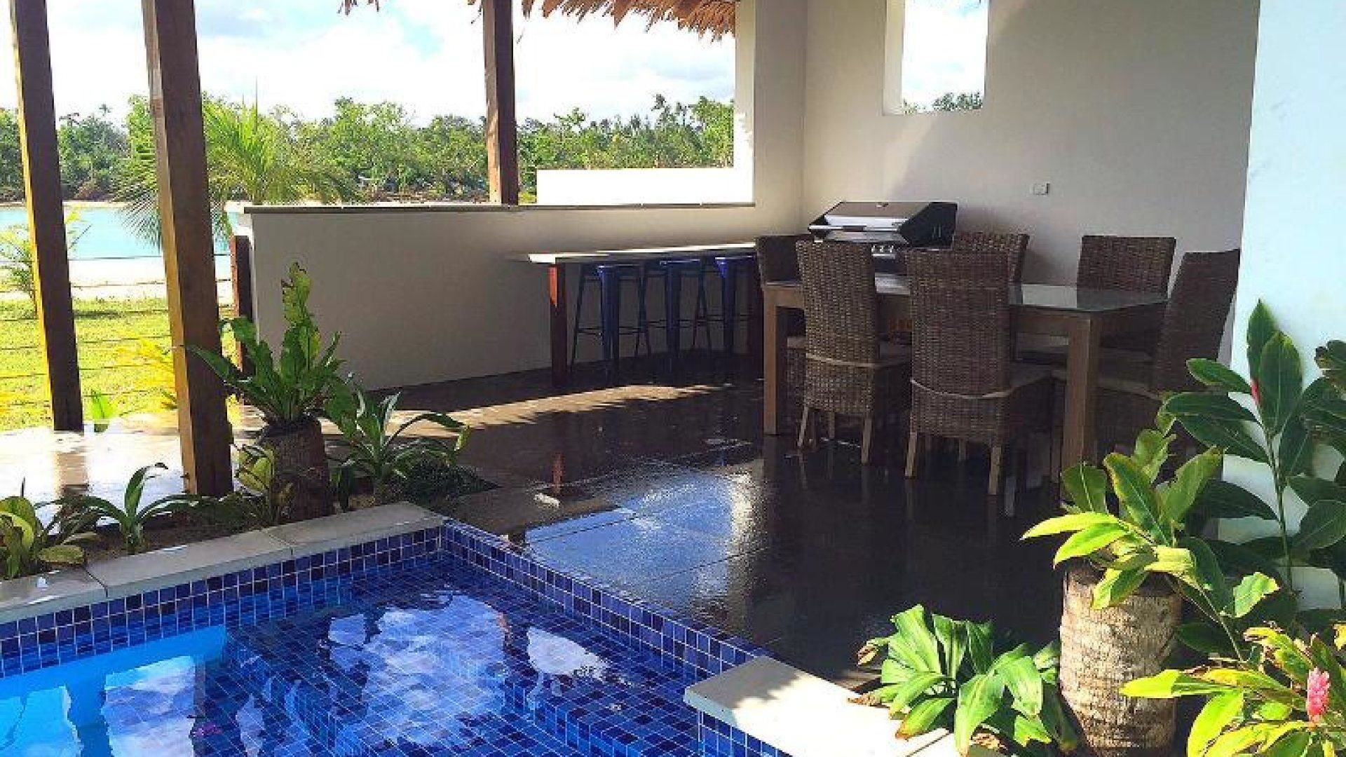 A pool area with a tiled edge, a grill, and wicker furniture.