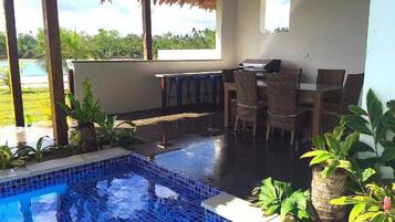 A pool area with a tiled edge, a grill, and wicker furniture.
