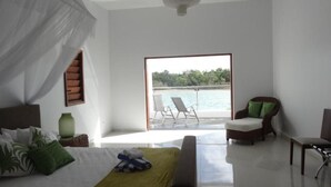 A bedroom with a large bed, a green throw blanket, a nightstand, and a window with a view of a balcony and water. - Paradise Point Views (Port Vila)