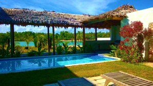 A pool area with a thatched roof structure, a pool, and surrounding greenery. - Paradise Point Views (Port Vila)
