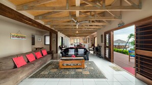 A spacious living area with a wooden ceiling, a black leather sofa with red cushions, a wooden coffee table, and a view of the beach through an open door. - Teouma Beachfront (Teouma)