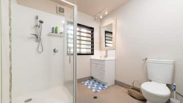 A modern bathroom with a glass-enclosed shower, a toilet, a sink with a mirror, and a window with blinds.