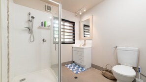 A modern bathroom with a glass-enclosed shower, a toilet, a sink with a mirror, and a window with blinds.
