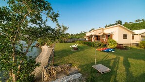 A house with a covered porch, a grassy yard, and a small pond. - Teouma Beachfront (Teouma)