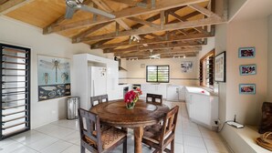 A spacious kitchen with a wooden ceiling, white cabinets, and a dining area with a round wooden table and chairs. - Teouma Beachfront (Teouma)