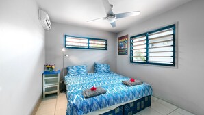 A bedroom with a bed, a ceiling fan, a window with blinds, a nightstand, and a wall-mounted air conditioner. - Teouma Beachfront (Teouma)