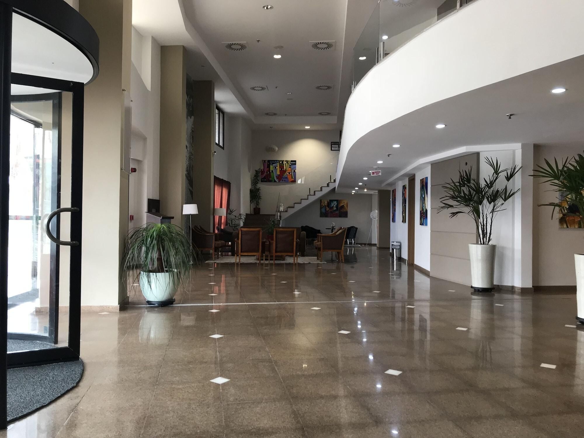 Un hall amplio con suelo pulido, una mesa de recepción, zona de estar y una escalera que conduce a un nivel superior.
