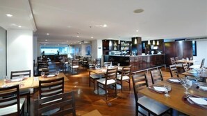 Ein geräumiges Restaurant mit mehreren Tischen, Stühlen, einer Bar und einer Küche im Hintergrund.
