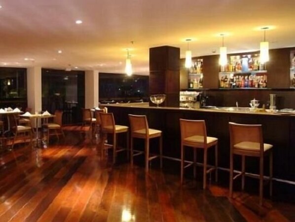 Un espace bar doté d’un plancher en bois, de tabourets de bar et de luminaires suspendus.