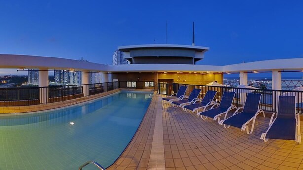 Ein Pool auf dem Dach mit Liegestühlen und Blick auf die Skyline der Stadt im Abendlicht.