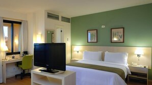 Ein Hotelzimmer mit einem Bett, einem Schreibtisch mit Computer, einem Fernseher und zwei Nachttischlampen.
