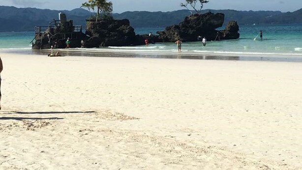 A beach with clear skies, rocky formations, and a few people. - El Puerto Boracay (Boracay Island)