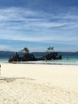 Une plage avec un ciel dégagé, des formations rocheuses et quelques personnes.
