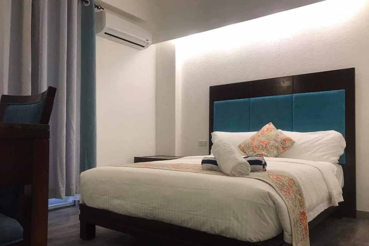 A hotel room with a bed, a nightstand, a chair, and a window with curtains.