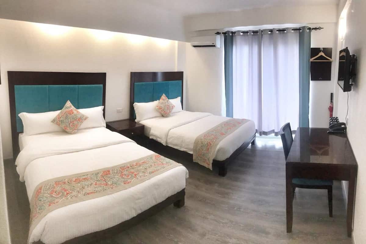A hotel room with two beds, a desk, and a chair.