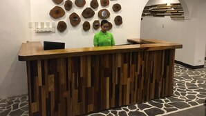 A reception desk with a wooden panel design, a woman standing behind it, and a wall decorated with circular wooden art pieces. - El Puerto Boracay (Boracay Island)