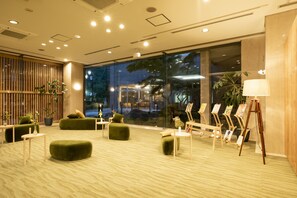 A modern lobby with green seating, a glass wall, and an easel with paintings. - Yutorelo Bandai Atami (Koriyama)