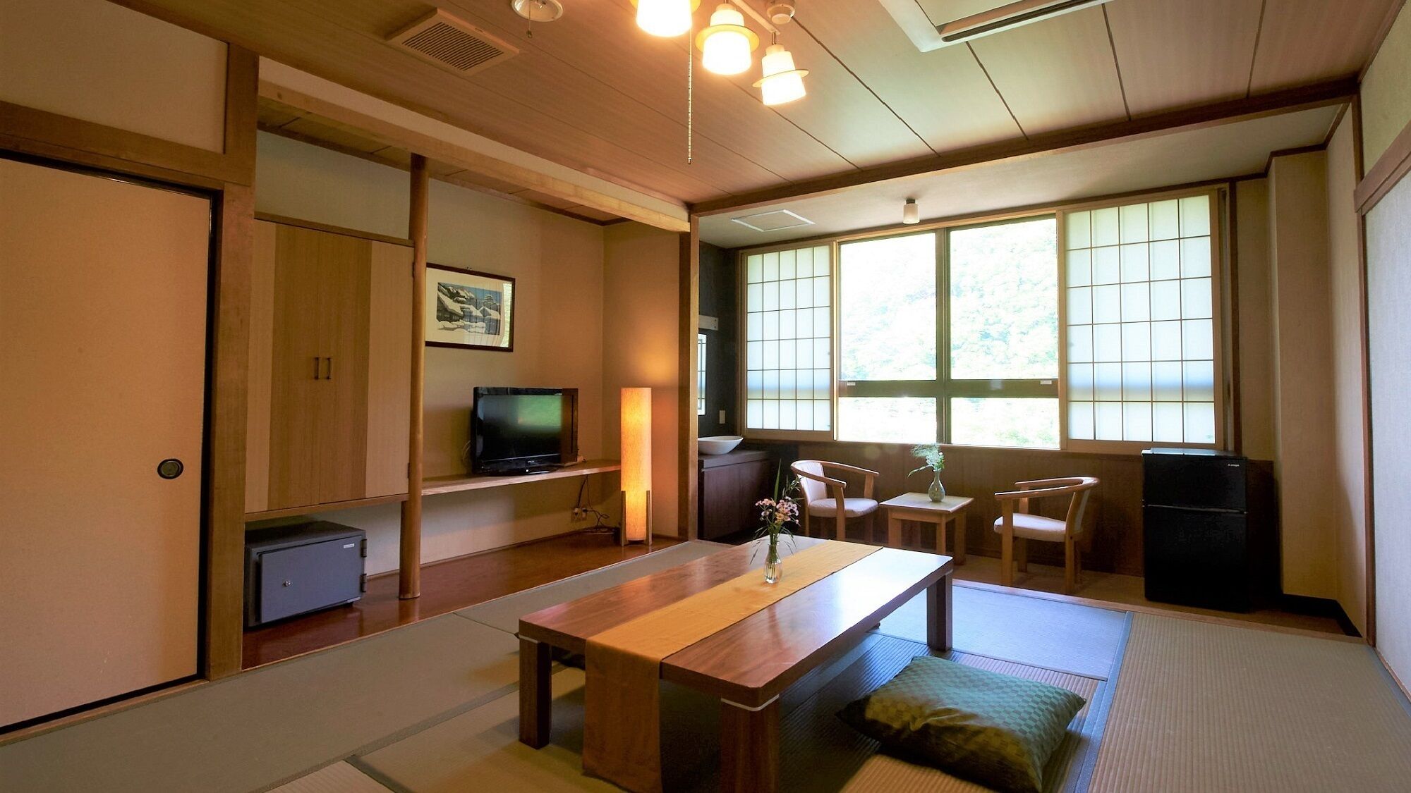 Een traditionele Japanse kamer met tatami vloerbedekking, een lage tafel, een televisie en schuifdeuren.