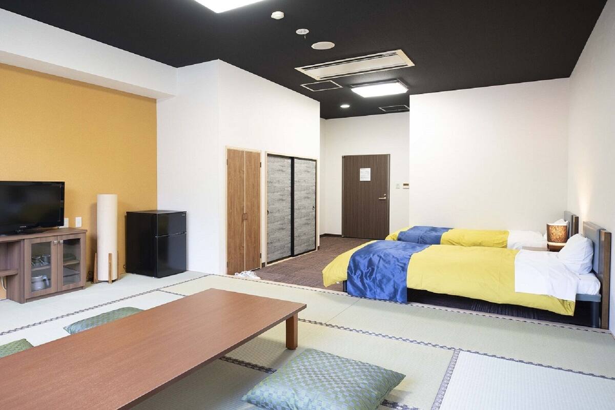 A hotel room with a bed, a television, a small refrigerator, a wooden cabinet, and a tatami mat floor.