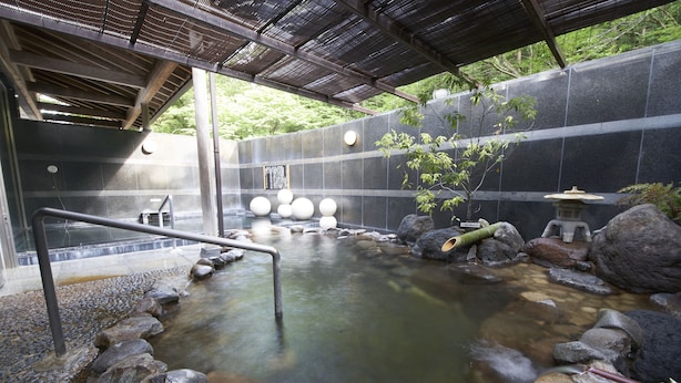 A traditional Japanese onsen with a stone bath, wooden steps, and a bamboo water spout.
