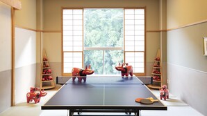A ping pong table with two red animal-shaped paddles, a net, and a window with a view of trees.
