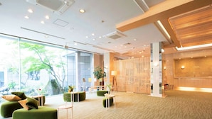 A modern lobby with green seating, a reception desk, and large windows overlooking a garden.