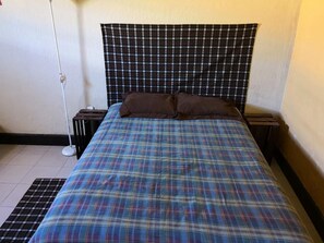 Une chambre à coucher avec une couvre-lit à carreaux, deux oreillers, une table de chevet et une lampe sur pied.