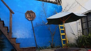 A blue wall with a wooden staircase, a metal ladder, and a round table with an umbrella. - Casa Azul (Guatemala City)
