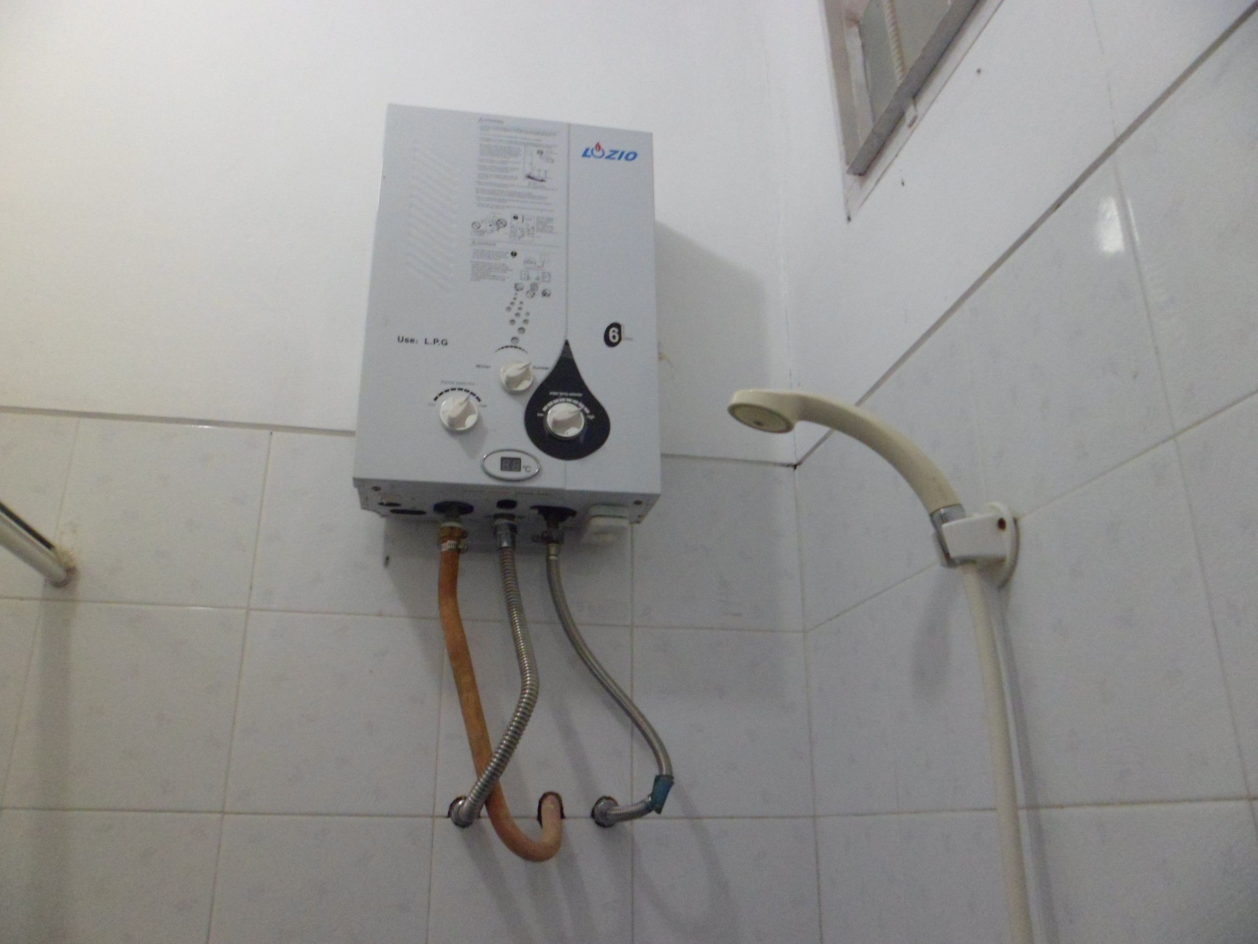 A water heater with control knobs and a digital display, connected to a showerhead.