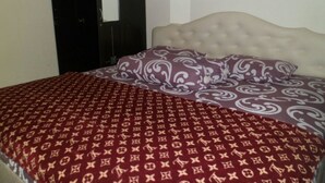 Een bed met een bedsprei met patroon en kussens, een gestoffeerd hoofdbord en een gedeeltelijk open deur.