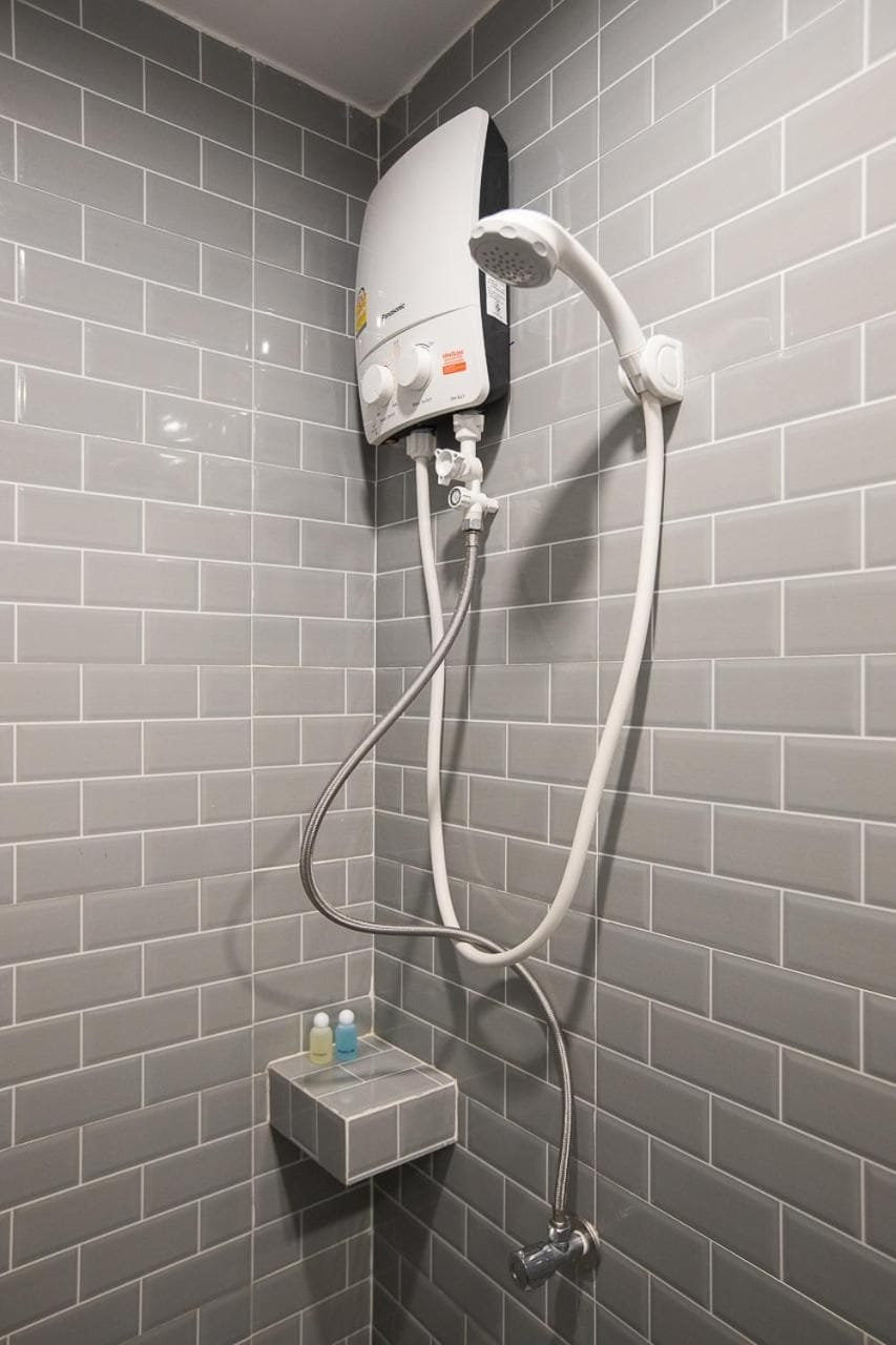 A shower with a handheld showerhead and a wall-mounted control panel.