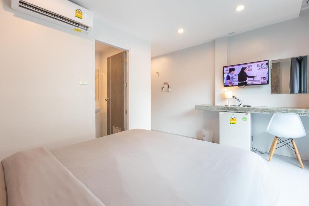 A hotel room with a bed, a desk with a chair, a television, and an air conditioning unit.