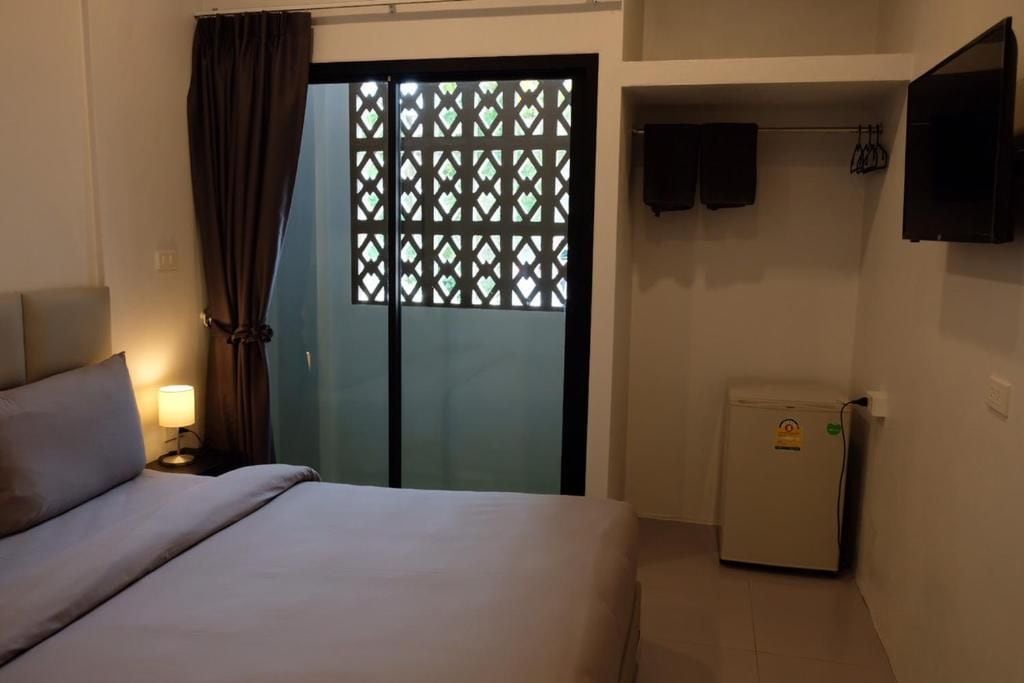 Una camera d'hotel con un letto, un comodino con una lampada, un frigorifero, una porta scorrevole con decorazioni a reticolo e una TV fissata al muro.
