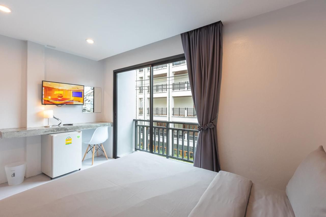 Une chambre d’hôtel équipée d’un lit, d’un bureau, d’une télévision et d’un balcon donnant sur un immeuble.