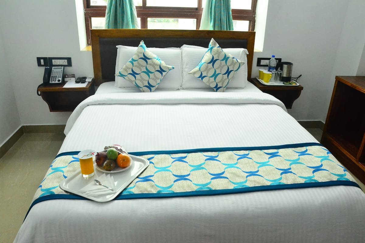 A neatly made bed with a blue and white patterned bedspread, a tray with breakfast items, and a bedside table with a phone and a water bottle.